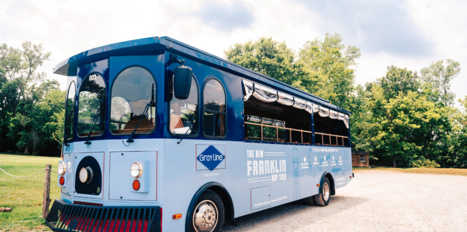 Things To Do A blue trolley-style tour bus with open sides and a canopy is parked on a gravel path in Williamson County, Tennessee.