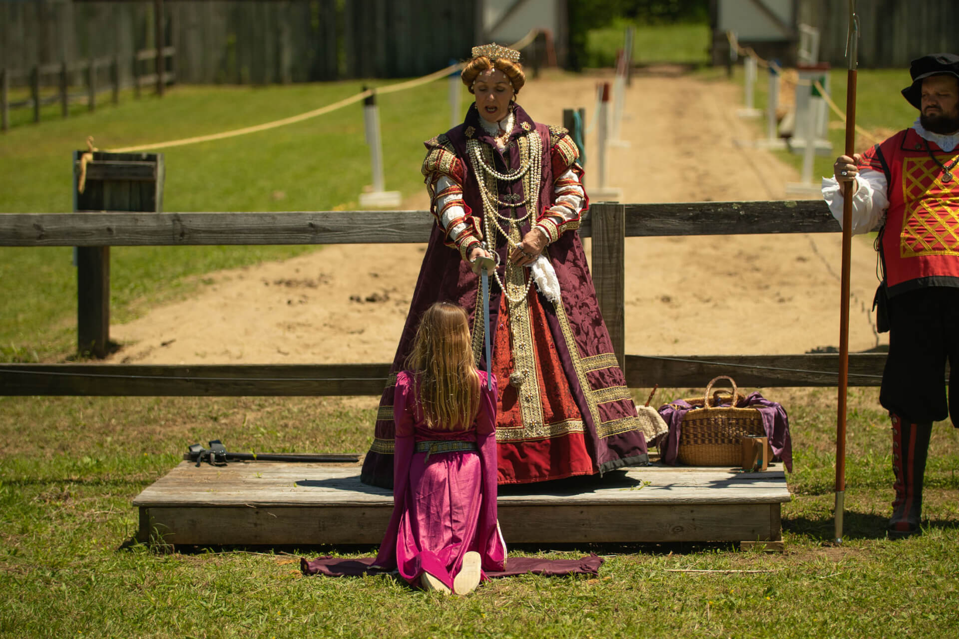 A woman dressed in a richly embroidered Renaissance gown kneels before a figure in regal attire, offering a sword as part of a historical reenactment ceremony in Williamson County, Tennessee.