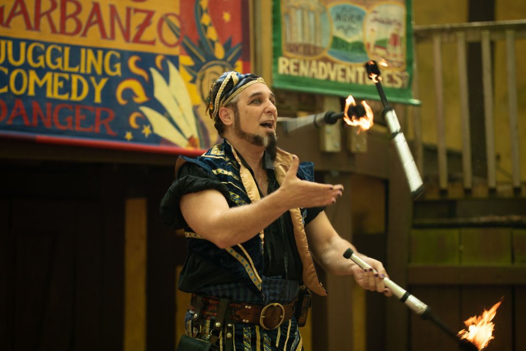 A man dressed in a colorful, medieval-inspired outfit juggles three flaming torches with skill and flair in Williamson County, Tennessee.