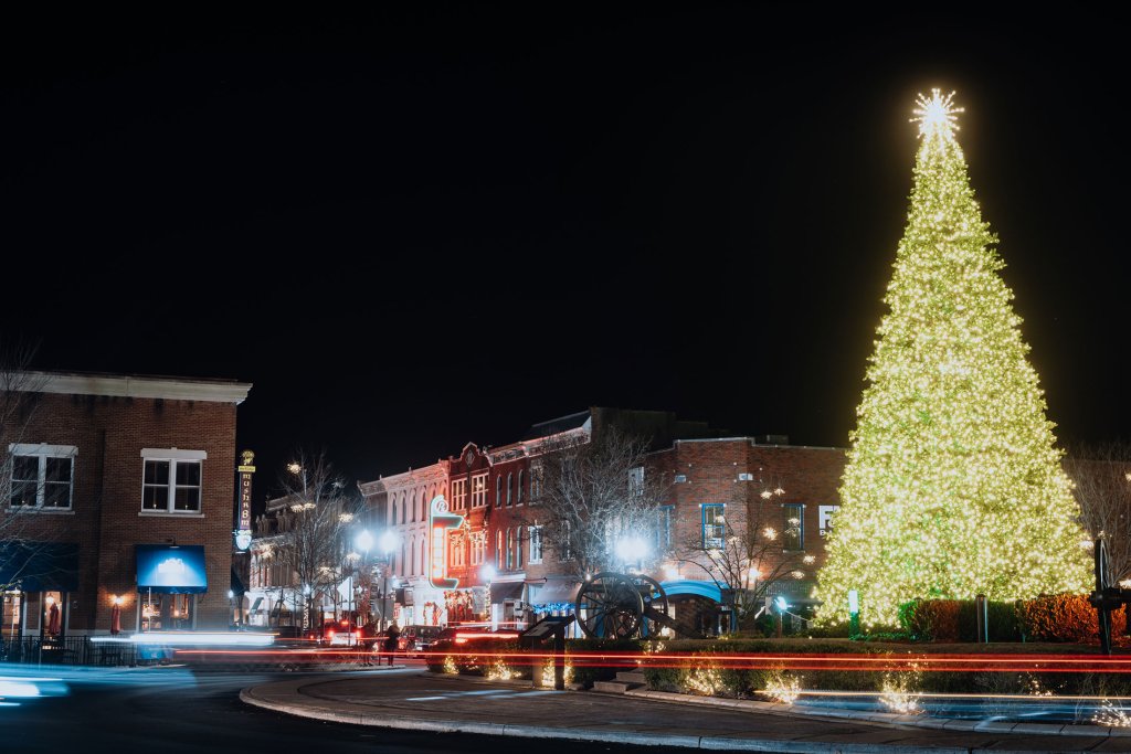 A beautifully lit Christmas tree stands tall in the center of a quaint town square, surrounded by historic brick buildings and twinkling streetlights in Williamson County, Tennessee.