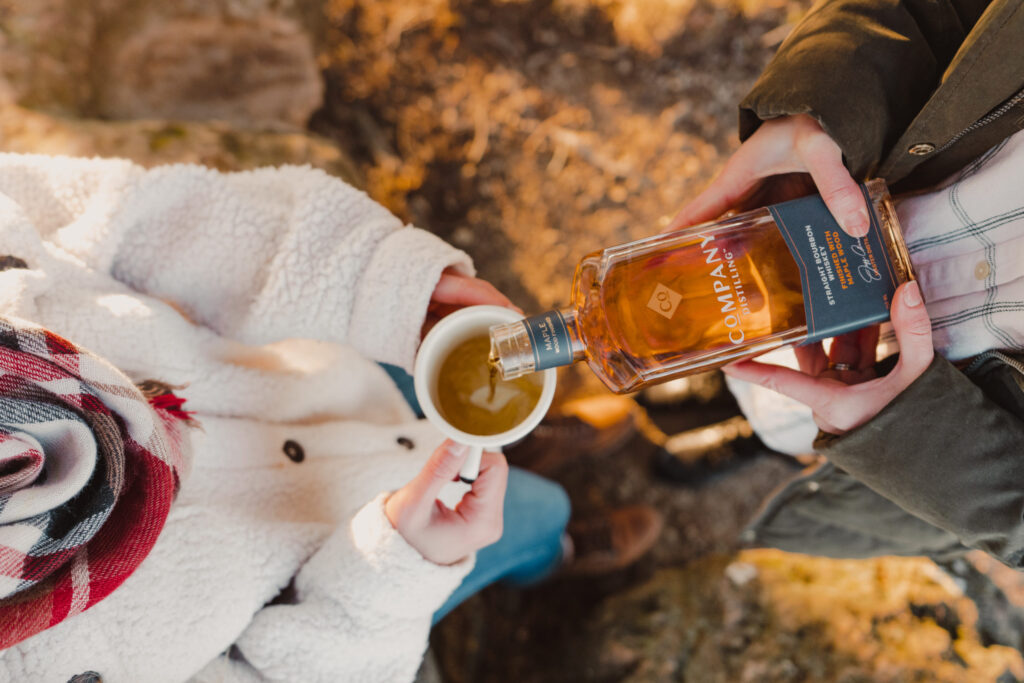 Two people share a moment, pouring whiskey into a mug on a rocky outcrop in Williamson County, Tennessee.