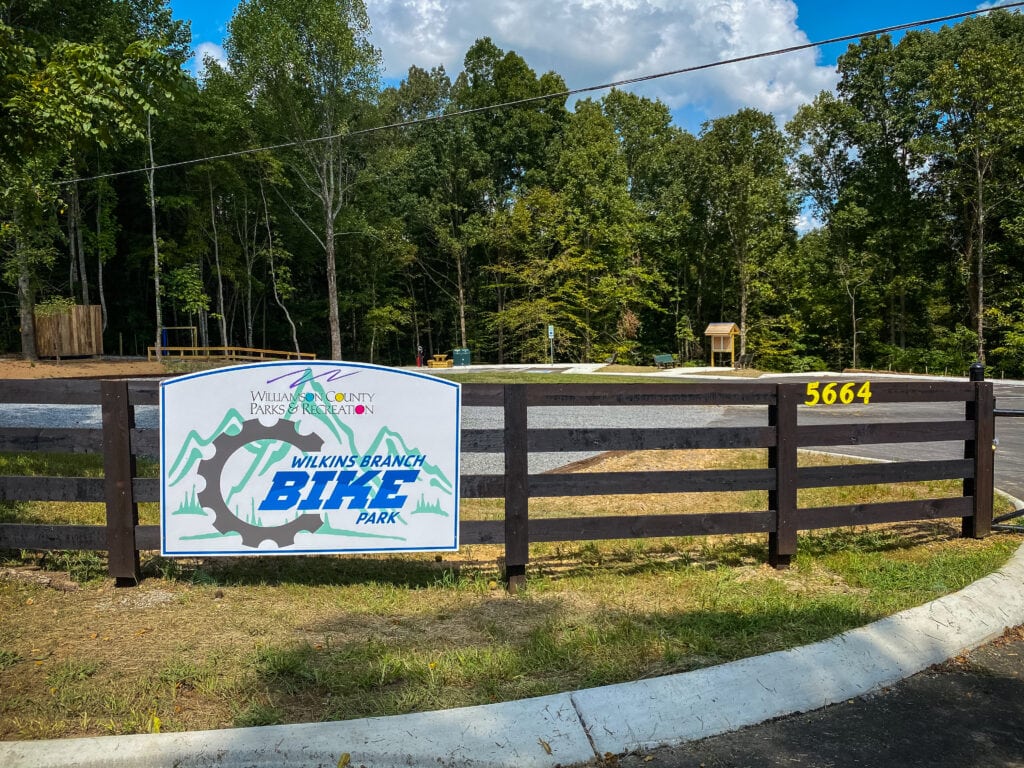 A wooden fence with a colorful sign advertising a bike park in a forested area in Williamson County, Tennessee.