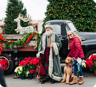 Dickens of a Christmas Santa Claus, accompanied by a woman and two dogs, stands beside a decorated truck and Christmas tree in Williamson County, Tennessee.
