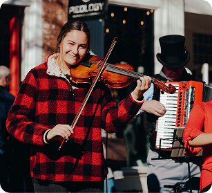 Dickens of a Christmas A young woman in a red and black plaid shirt plays the violin on the street, accompanied by a man in a top hat playing the accordion in Williamson County, Tennessee.