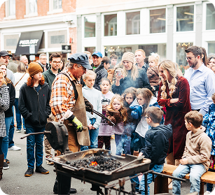 Dickens of a Christmas Crowd gathers around blacksmith demonstrating traditional metalworking techniques with fire and hammer in Williamson County, Tennessee.
