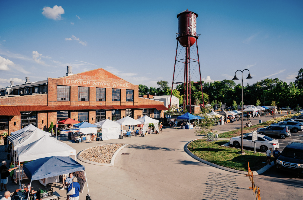 A bustling outdoor market with colorful tents and a historic red brick building featuring a water tower in the background in Williamson County, Tennessee.