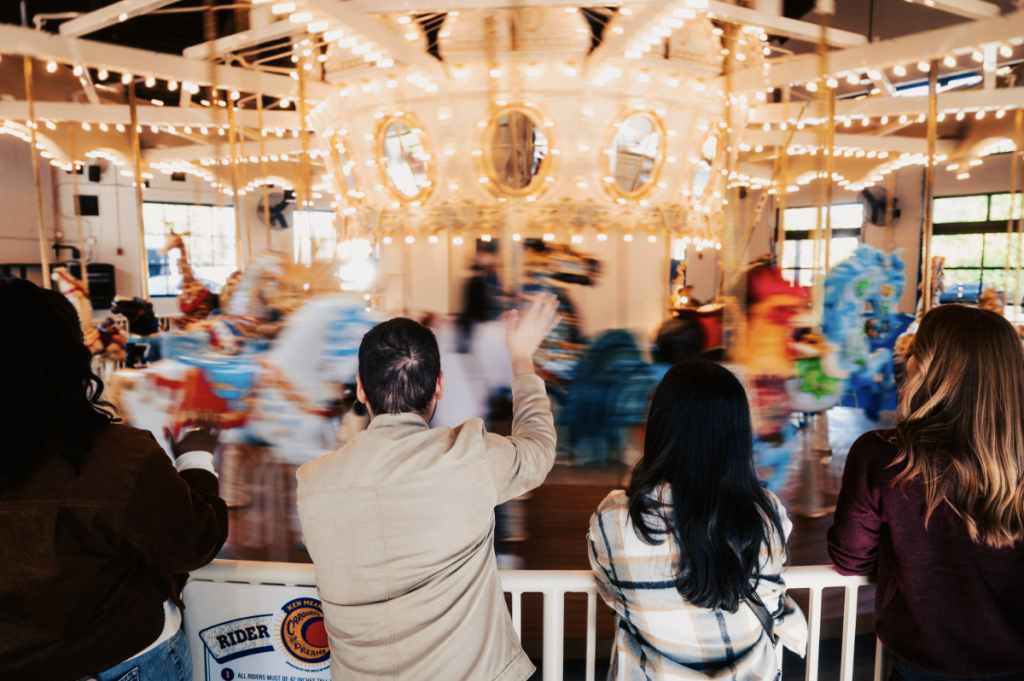 A group of people are gathered around a beautifully lit carousel, watching it spin with a mesmerizing blur of colors and lights in Williamson County, Tennessee.