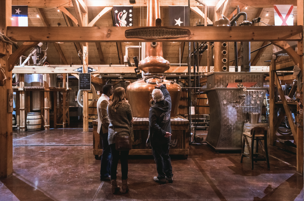 12 Amazing Things to Do in Charming Leiper's Fork, Tennessee Three people tour a distillery, examining a large copper still in a wooden-beamed warehouse in Williamson County, Tennessee.